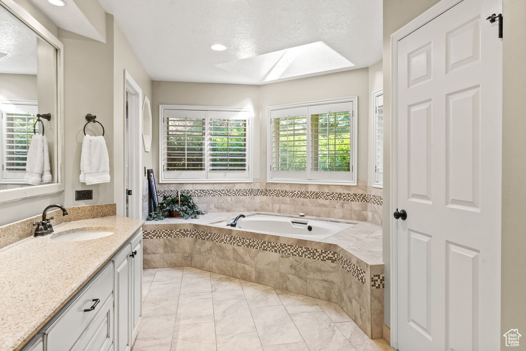 Bathroom with tiled bath, vanity with extensive cabinet space, a textured ceiling, and a skylight