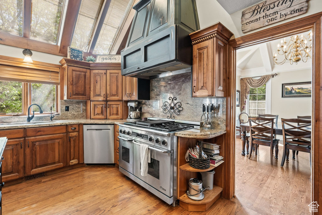 Kitchen with vaulted ceiling, light stone counters, backsplash, light wood-type flooring, and appliances with stainless steel finishes