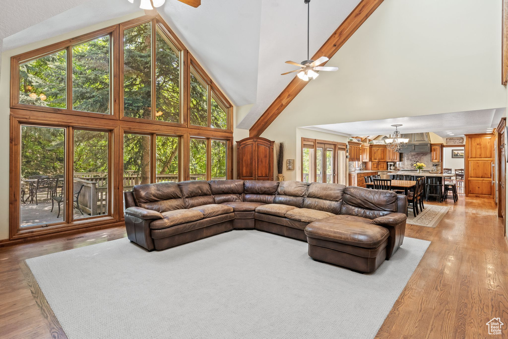 Living room with beamed ceiling, high vaulted ceiling, ceiling fan with notable chandelier, and light hardwood / wood-style flooring