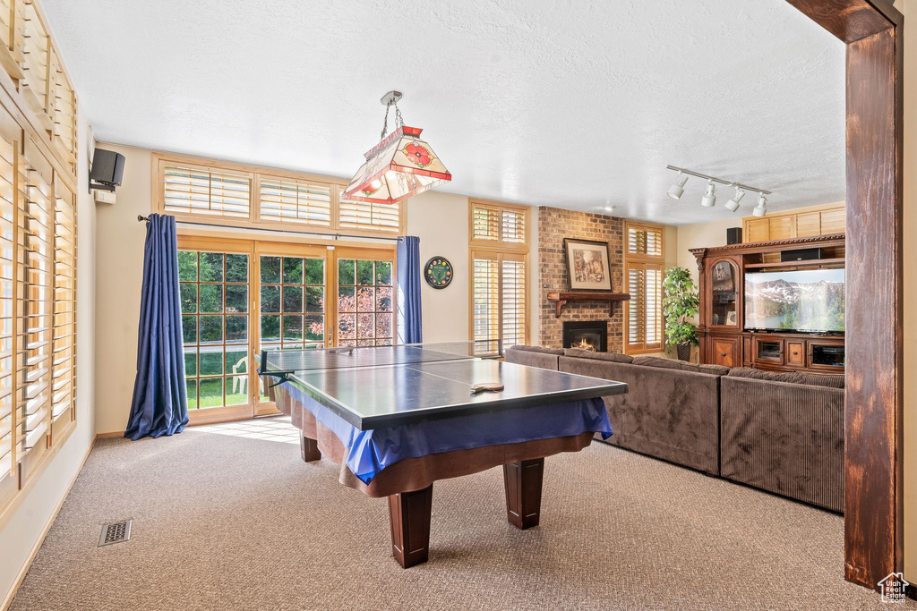 Rec room with a textured ceiling, a fireplace, brick wall, rail lighting, and carpet flooring