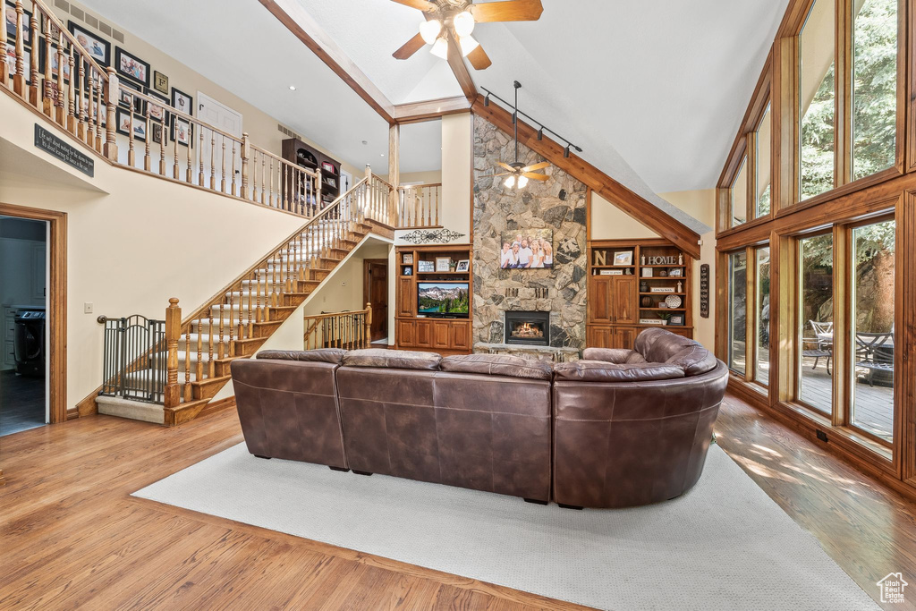 Living room featuring high vaulted ceiling, hardwood / wood-style floors, ceiling fan, and a fireplace