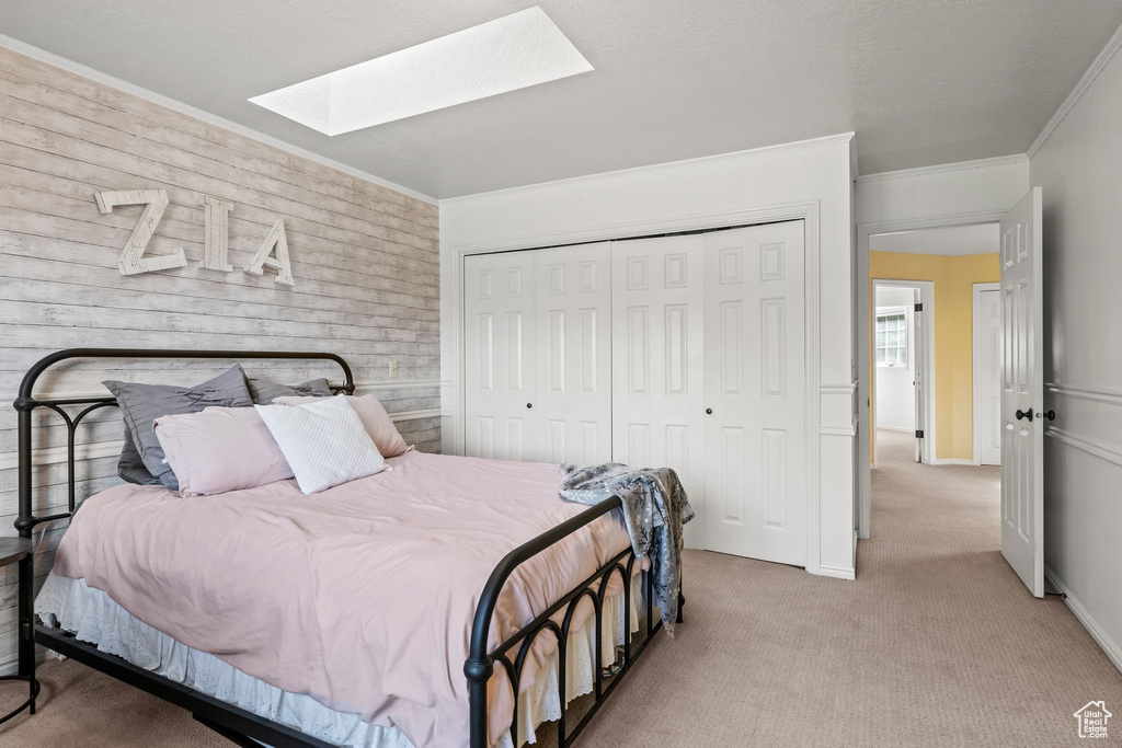 Bedroom featuring a closet, a skylight, wood walls, ornamental molding, and carpet floors