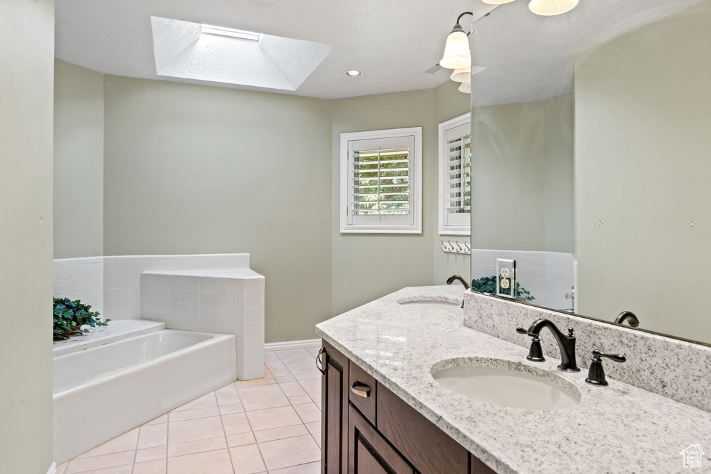 Bathroom with a tub, tile flooring, a skylight, and vanity