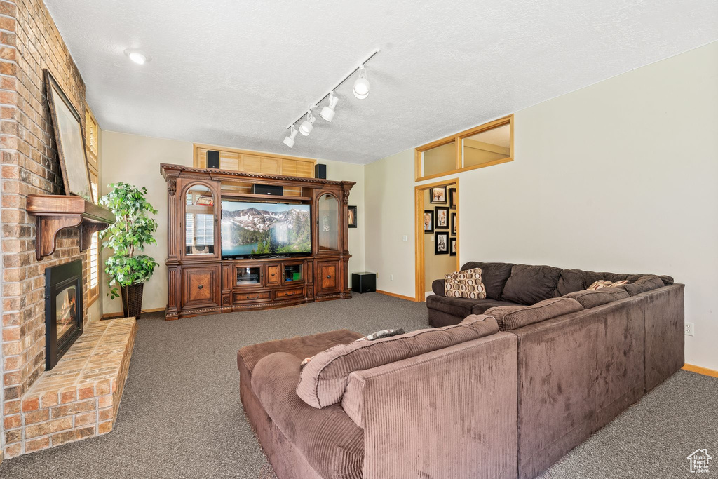 Carpeted living room featuring a textured ceiling, brick wall, a brick fireplace, and rail lighting