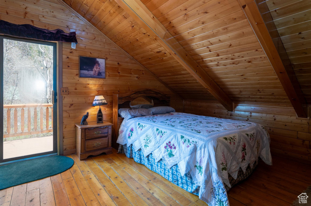 Bedroom featuring light hardwood / wood-style flooring, wood walls, vaulted ceiling with beams, and wooden ceiling