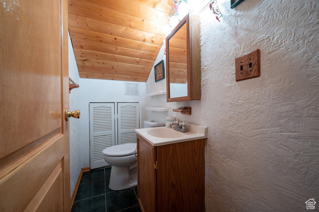 Bathroom with wooden ceiling, tile floors, vaulted ceiling, vanity with extensive cabinet space, and toilet