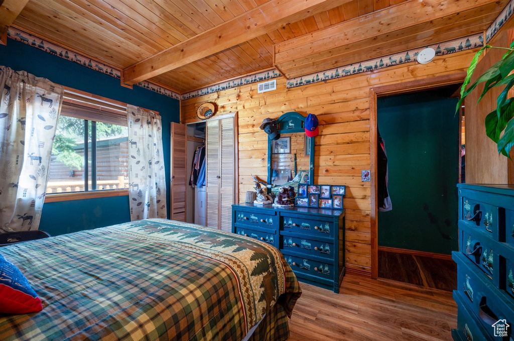 Bedroom with a closet, wood walls, hardwood / wood-style flooring, beam ceiling, and wood ceiling