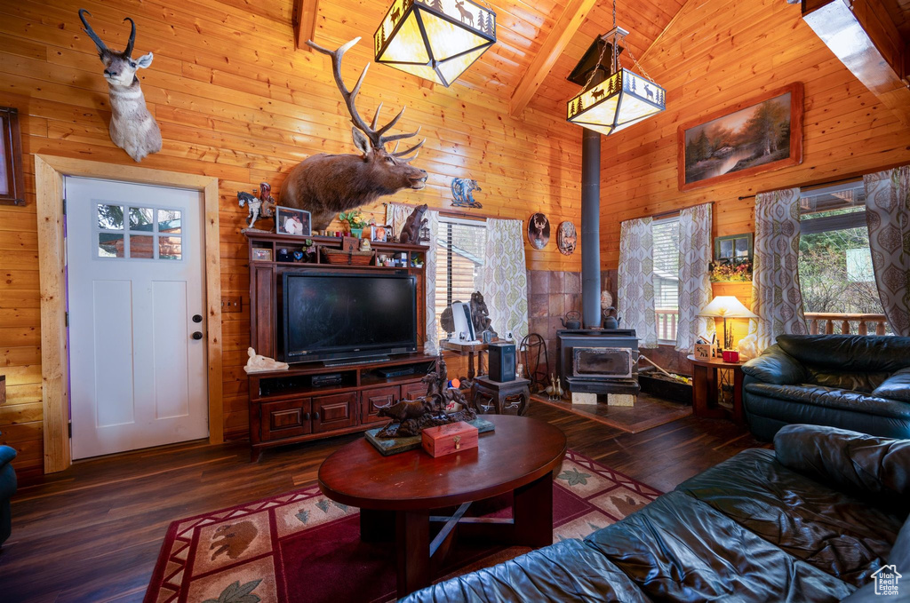 Living room featuring a wood stove, wood walls, wooden ceiling, hardwood / wood-style floors, and beam ceiling