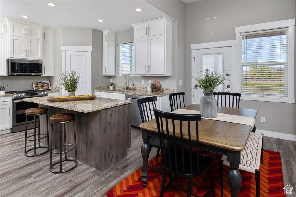 Kitchen featuring light hardwood / wood-style floors, white cabinets, a kitchen island, and appliances with stainless steel finishes