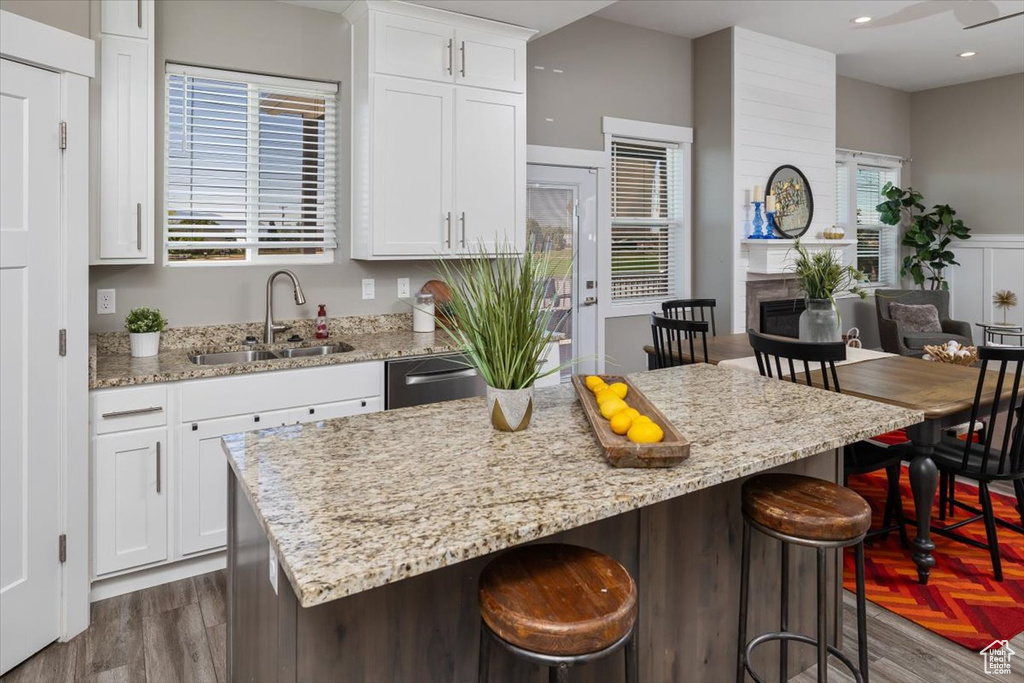 Kitchen featuring white cabinetry, a kitchen island, a breakfast bar area, light stone counters, and sink