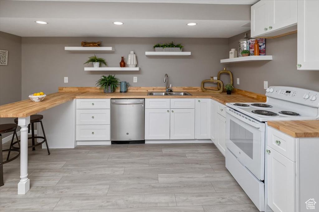 Kitchen featuring white range with electric stovetop, white cabinetry, stainless steel dishwasher, wooden counters, and sink