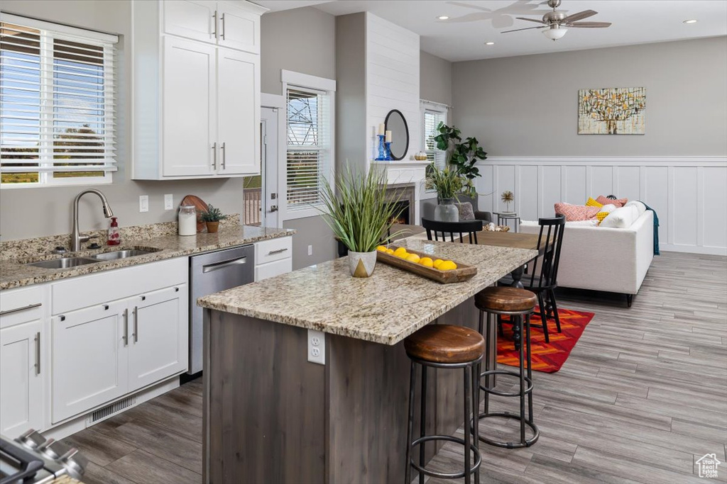 Kitchen featuring a center island, white cabinetry, wood-type flooring, a large fireplace, and ceiling fan