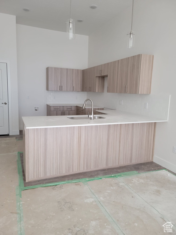 Kitchen with light brown cabinets, sink, a towering ceiling, and pendant lighting