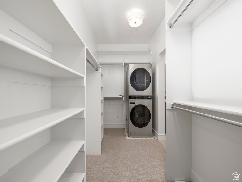 Walk in closet with light colored carpet and stacked washer and clothes dryer