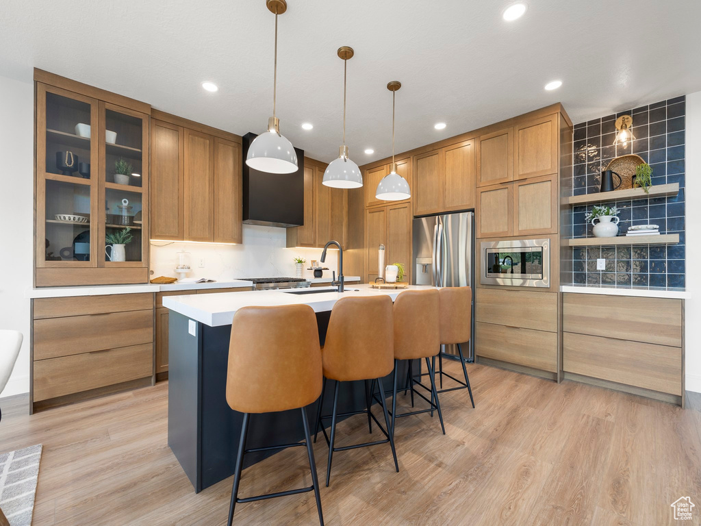 Kitchen with decorative light fixtures, a kitchen island with sink, light wood-type flooring, appliances with stainless steel finishes, and sink