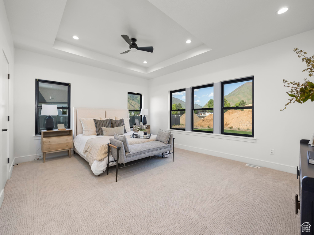 Bedroom featuring a raised ceiling, ceiling fan, and light colored carpet