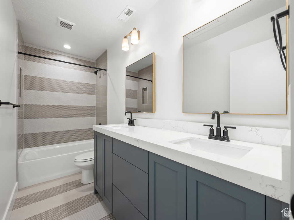 Full bathroom featuring tile floors, dual bowl vanity, toilet, and tiled shower / bath