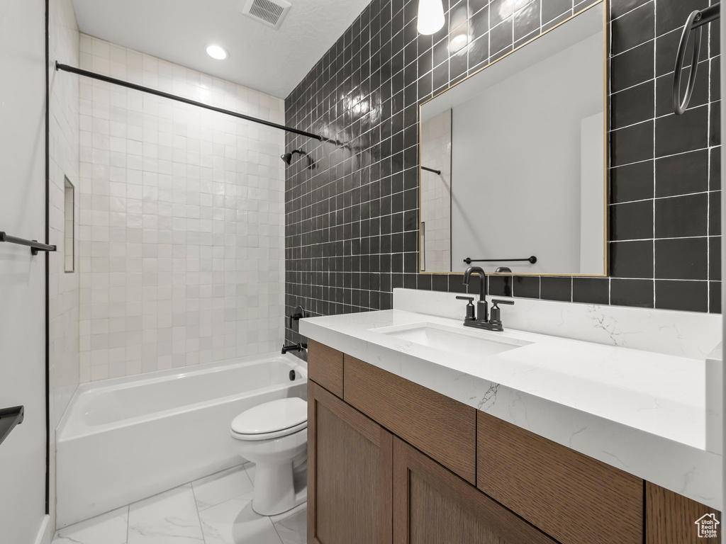 Full bathroom featuring tile flooring, vanity with extensive cabinet space, tile walls, tiled shower / bath, and toilet