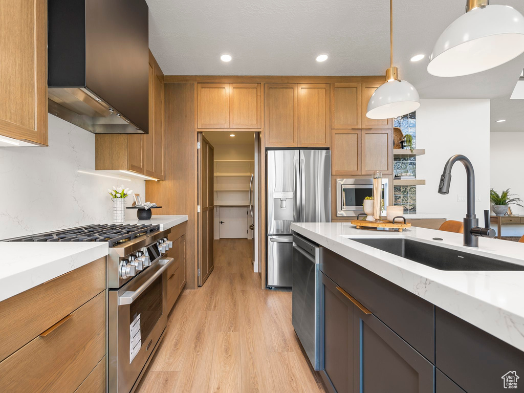 Kitchen with light hardwood / wood-style floors, stainless steel appliances, wall chimney exhaust hood, decorative light fixtures, and sink