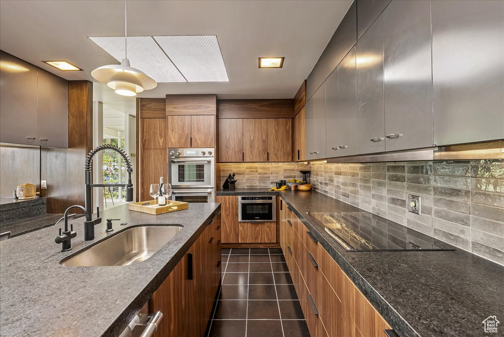 Kitchen with a skylight, hanging light fixtures, tasteful backsplash, dark tile flooring, and sink