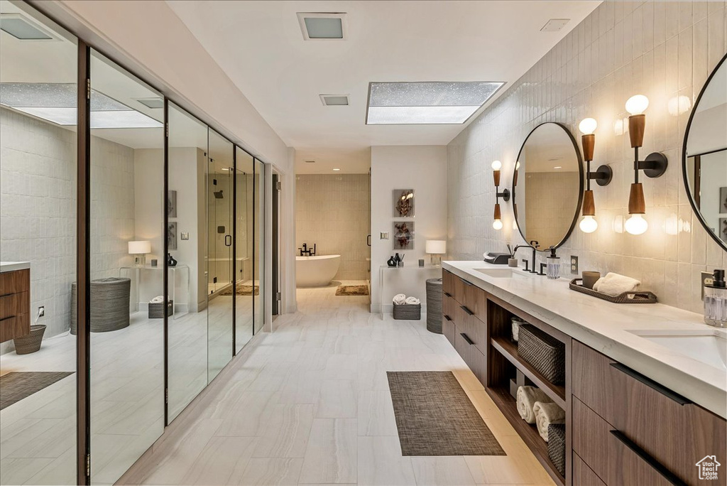 Bathroom with a bath to relax in, tile flooring, double sink vanity, and tile walls