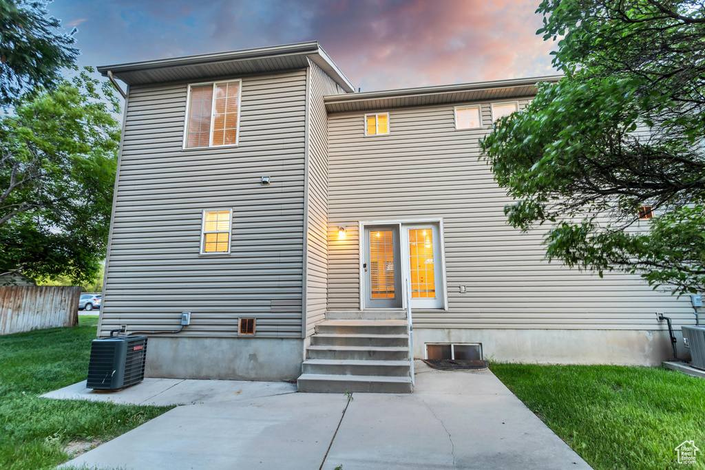 Back house at dusk featuring a patio, a yard, and central air condition unit