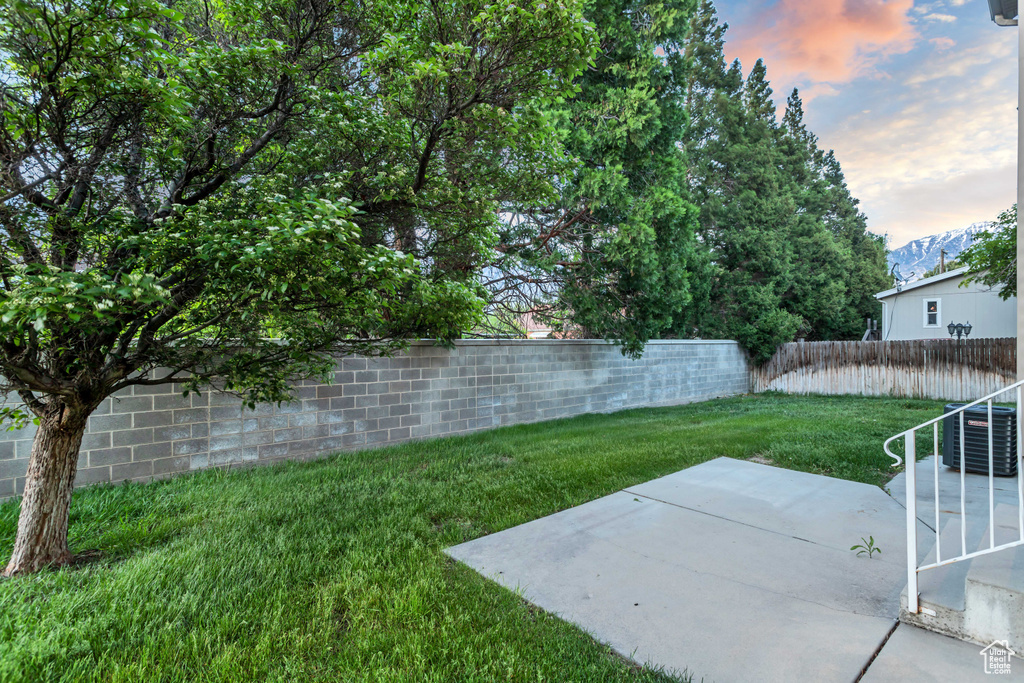 Yard at dusk with central air condition unit and a patio