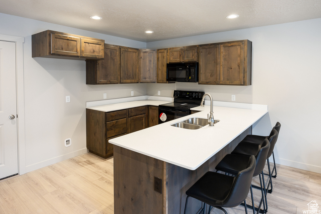 Kitchen with light hardwood / wood-style flooring, kitchen peninsula, black appliances, sink, and a breakfast bar area