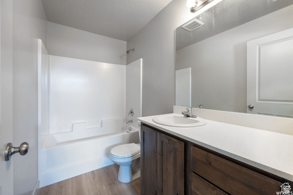 Full bathroom featuring toilet, tub / shower combination, wood-type flooring, vanity, and a textured ceiling