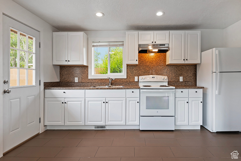 Kitchen with sink, white cabinets, white appliances, and dark tile floors