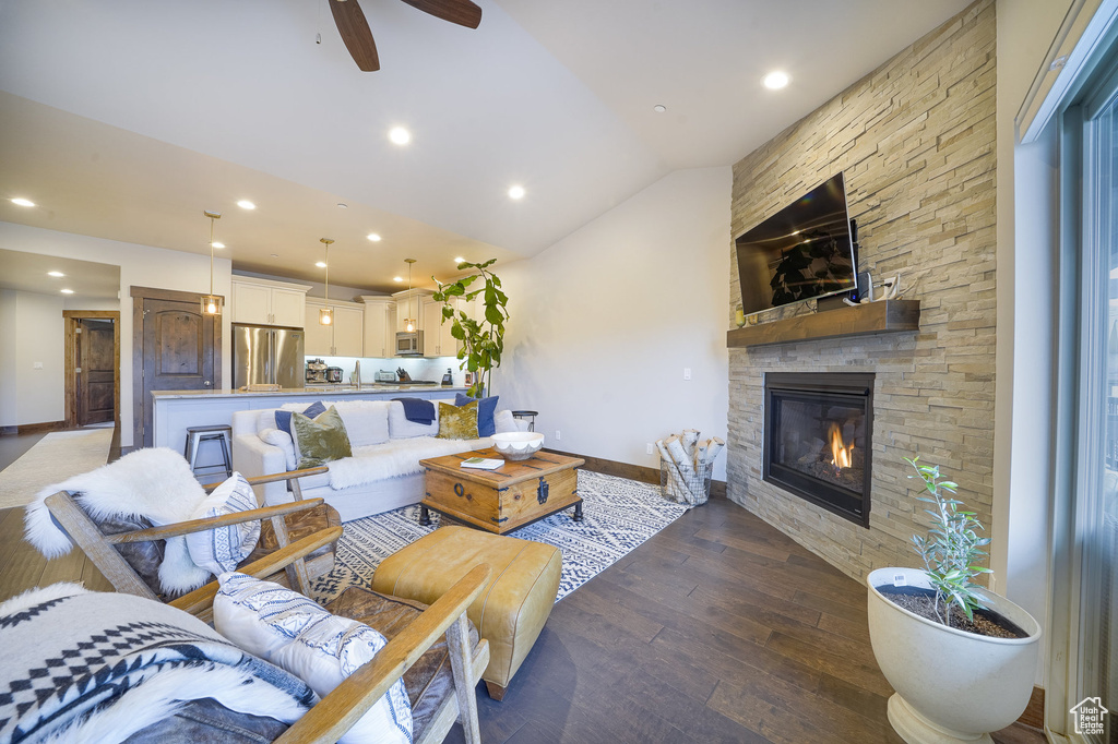 Living room featuring a stone fireplace, lofted ceiling, dark wood-type flooring, and ceiling fan