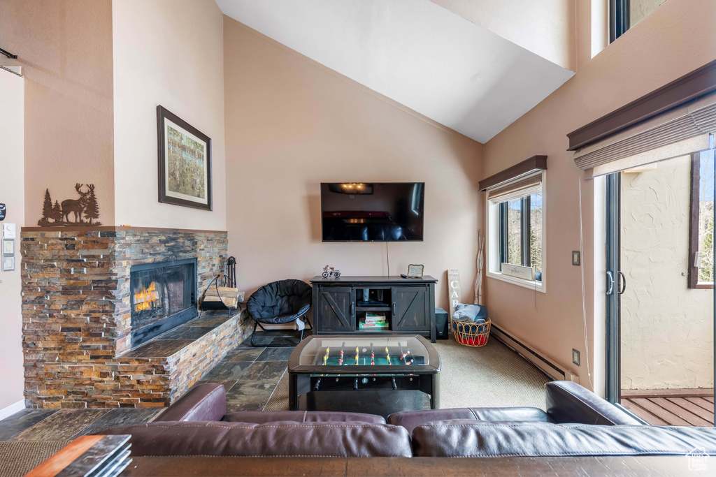 Carpeted living room featuring high vaulted ceiling, a stone fireplace, and a baseboard radiator