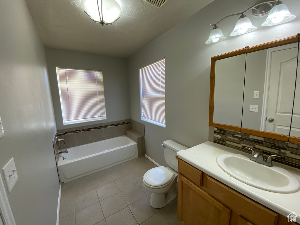 Bathroom with backsplash, toilet, tile floors, a washtub, and vanity