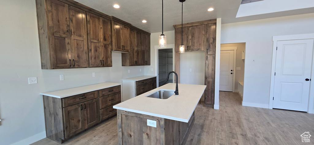 Kitchen with light hardwood / wood-style floors, decorative light fixtures, dark brown cabinetry, and sink