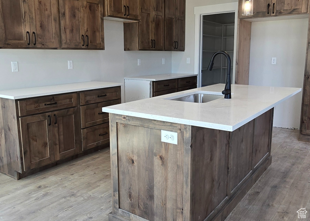 Kitchen featuring dark brown cabinetry, sink, light hardwood / wood-style flooring, and an island with sink