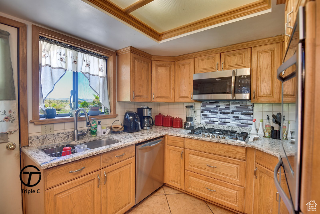 Kitchen featuring tasteful backsplash, light stone countertops, appliances with stainless steel finishes, sink, and light tile floors