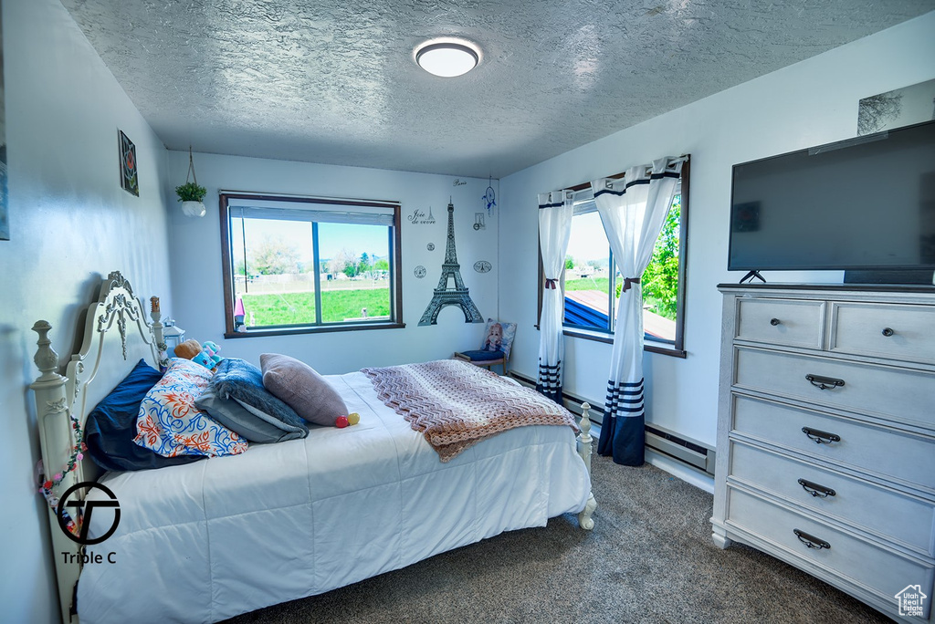 Carpeted bedroom featuring a textured ceiling and baseboard heating