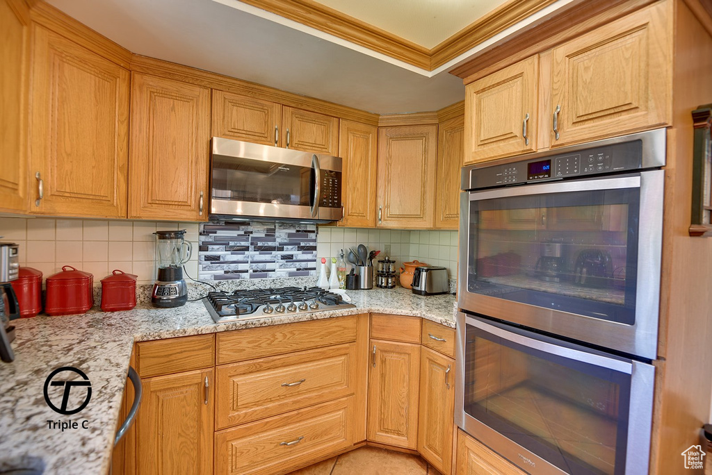 Kitchen featuring light stone countertops, tasteful backsplash, ornamental molding, and stainless steel appliances