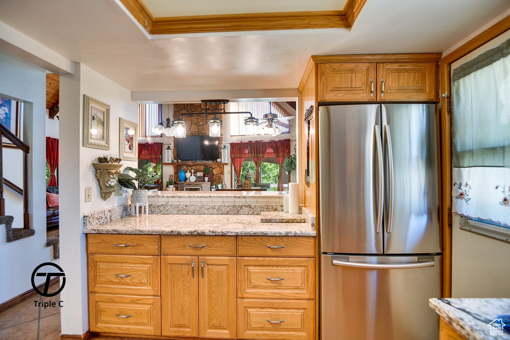 Kitchen with light tile flooring, stainless steel fridge, light stone counters, and a raised ceiling
