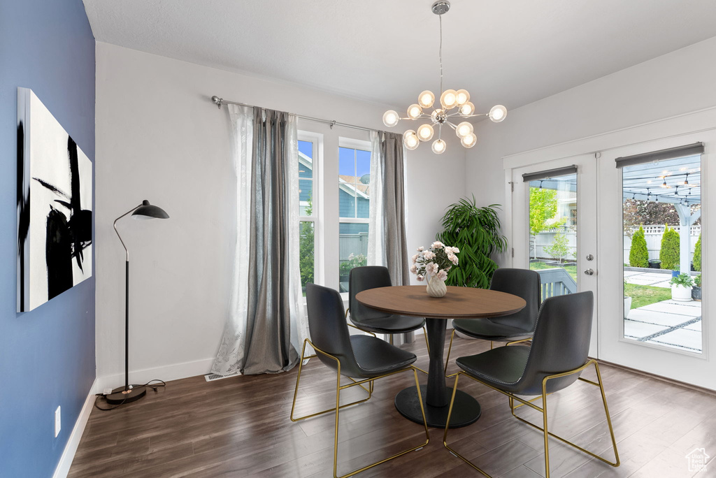 Dining space with dark wood-type flooring, an inviting chandelier, and french doors