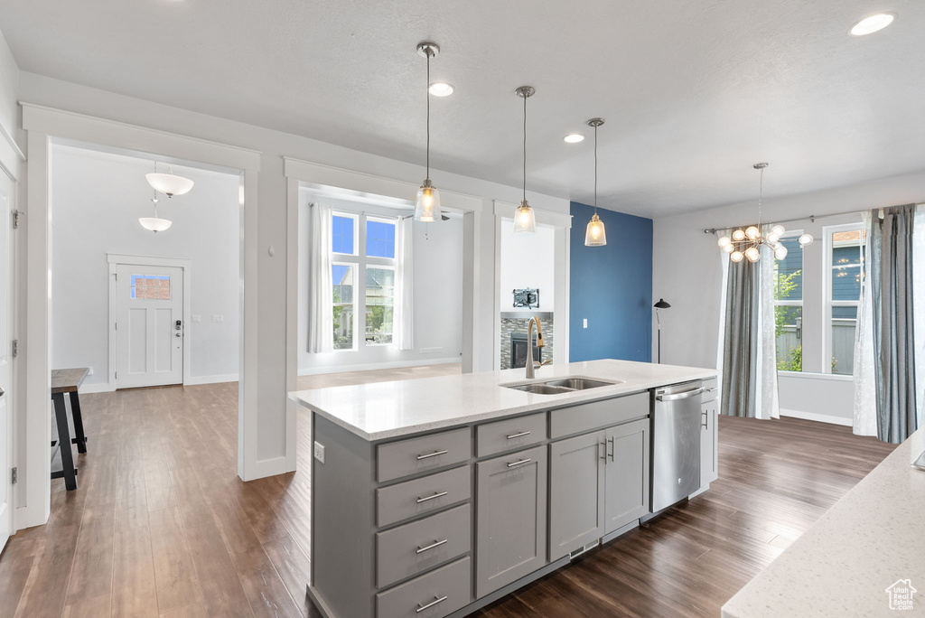 Kitchen with hanging light fixtures, dark wood-type flooring, a center island with sink, and stainless steel dishwasher