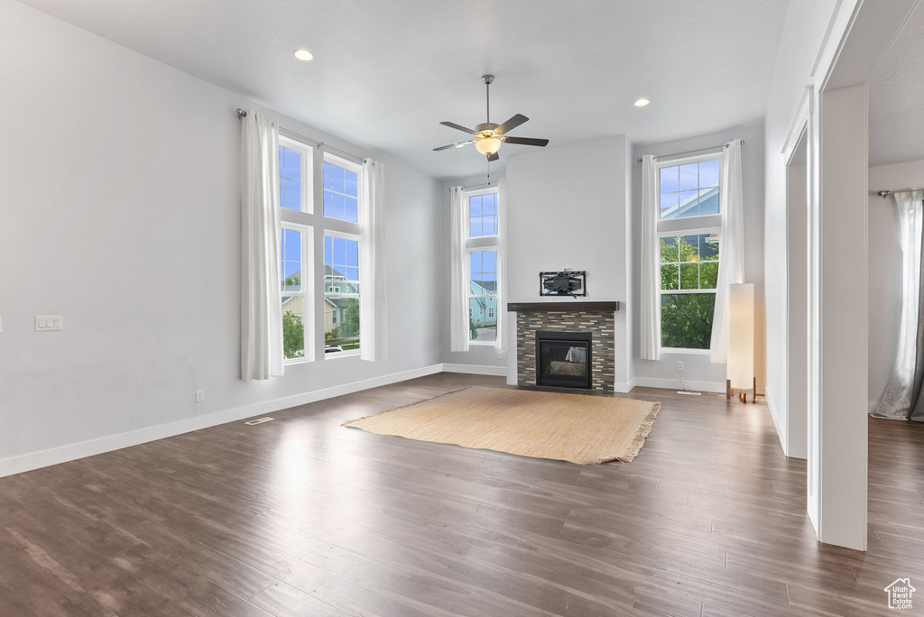 Unfurnished living room with dark hardwood / wood-style flooring, plenty of natural light, ceiling fan, and a fireplace