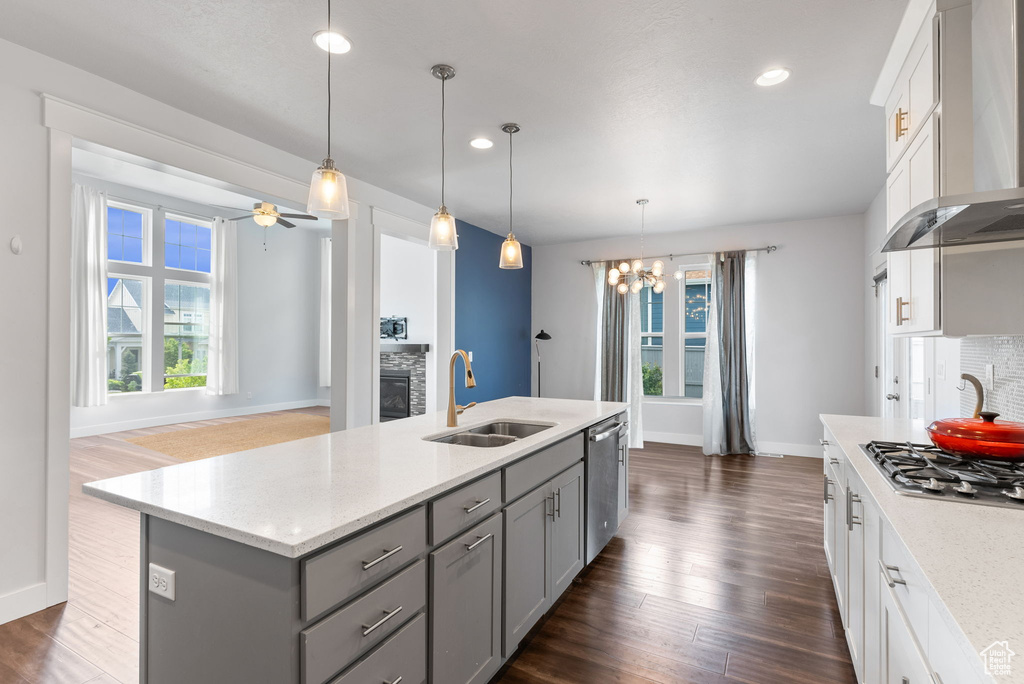 Kitchen featuring dark wood-type flooring, pendant lighting, a center island with sink, and wall chimney exhaust hood