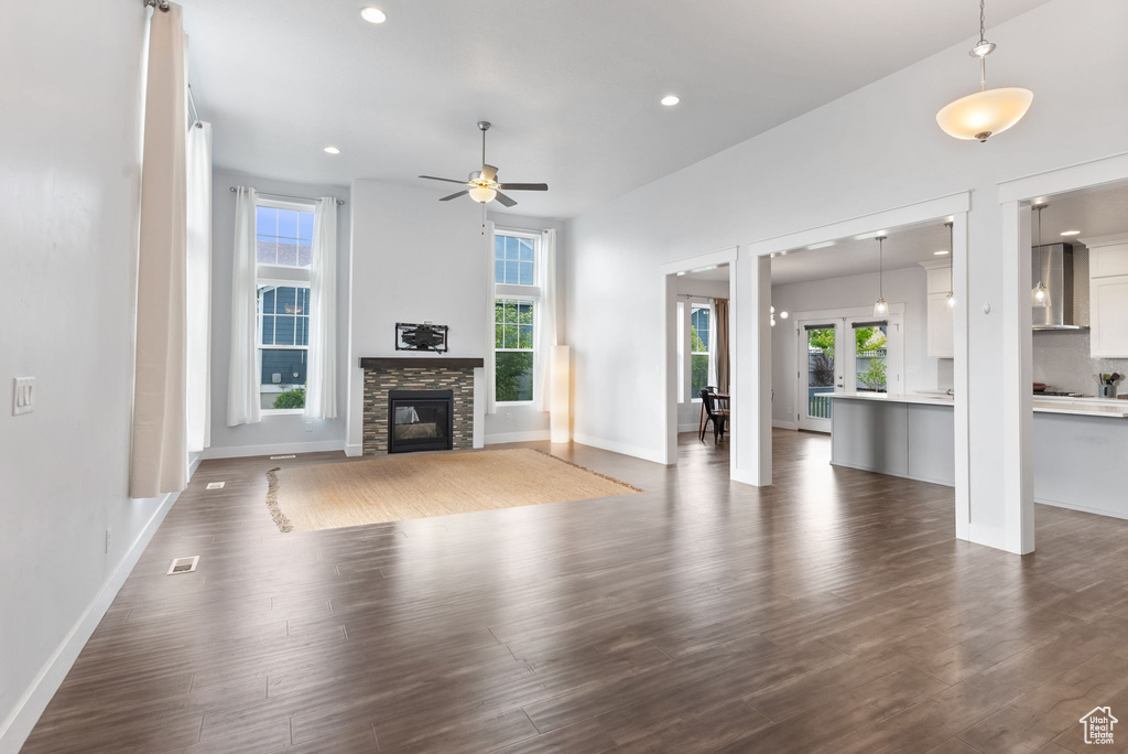 Unfurnished living room with a healthy amount of sunlight, ceiling fan, a fireplace, and dark hardwood / wood-style floors