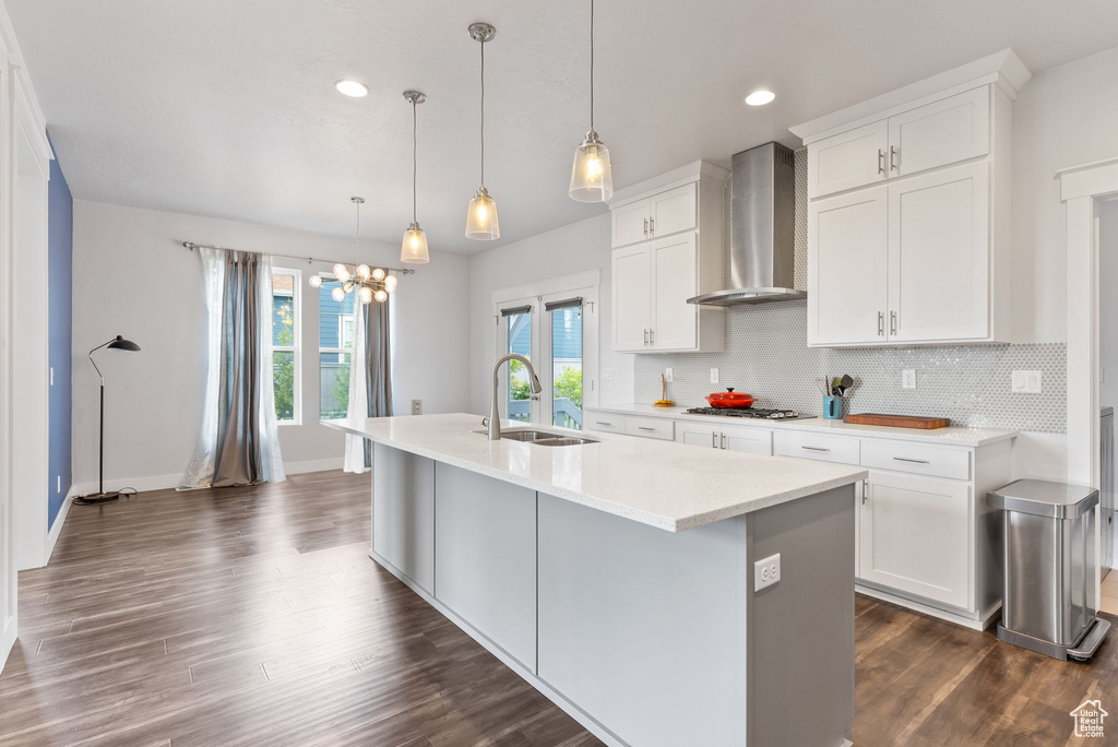 Kitchen with wall chimney range hood, dark hardwood / wood-style floors, backsplash, hanging light fixtures, and sink