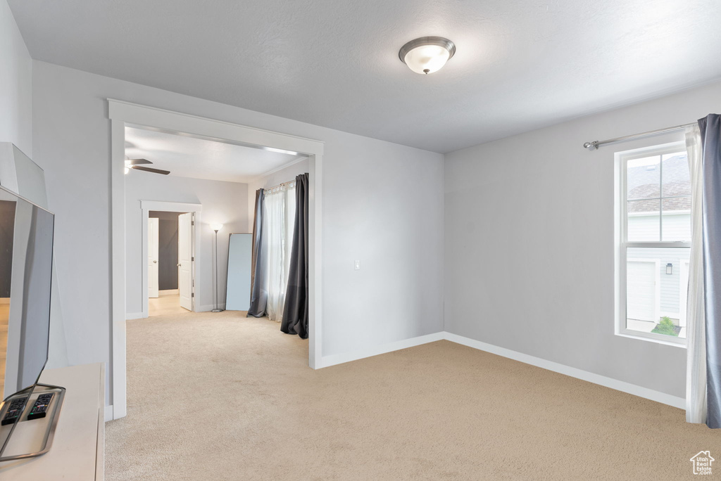 Spare room with ceiling fan, a wealth of natural light, and light carpet