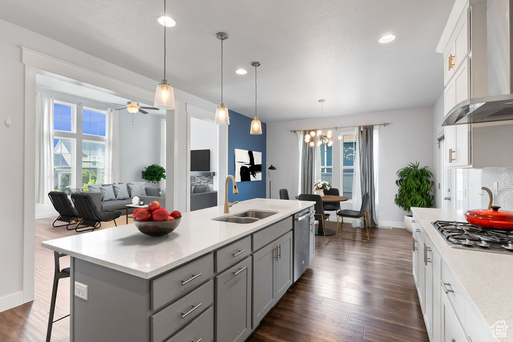 Kitchen featuring wall chimney range hood, sink, dark hardwood / wood-style floors, and a center island with sink