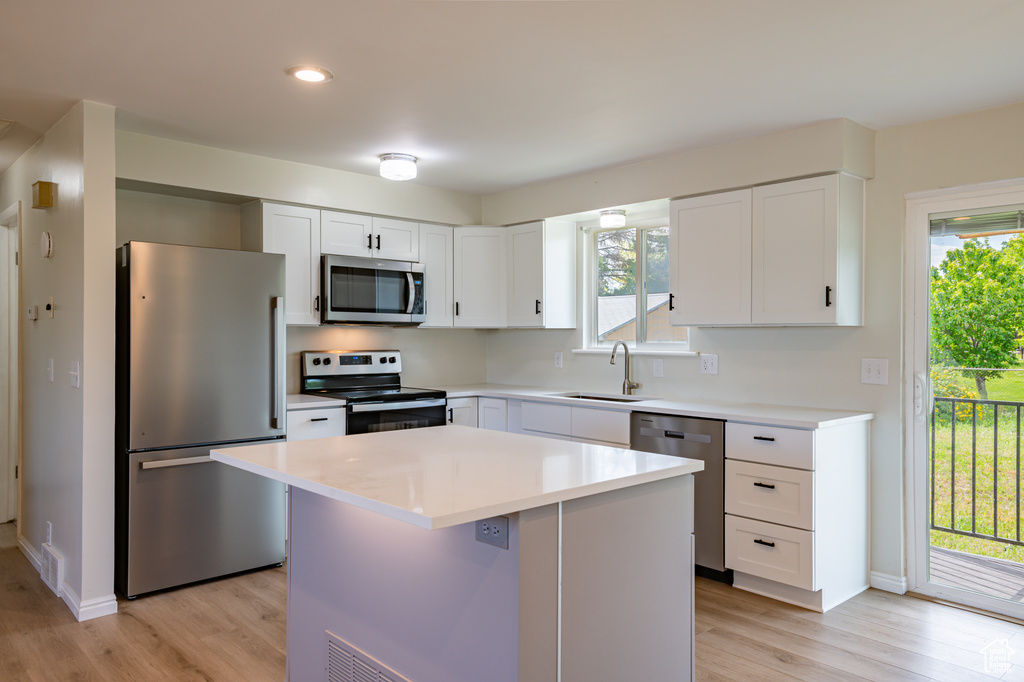 Kitchen with light hardwood / wood-style floors, a healthy amount of sunlight, a kitchen island, and appliances with stainless steel finishes