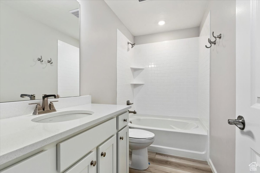 Full bathroom with toilet, vanity, tiled shower / bath, and hardwood / wood-style floors