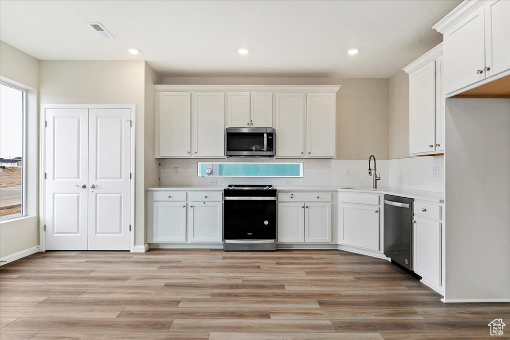 Kitchen featuring white cabinetry, light wood-type flooring, stainless steel appliances, backsplash, and sink